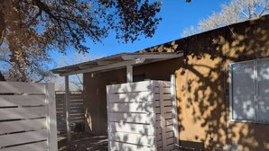 A fenced outdoor area with a pergola, a building with a window, and a tree casting shadows. - Downtown District Modern Apt - Yard - WiFi - King (Albuquerque)