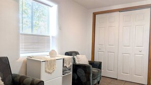 A room with a white cabinet, a grey armchair, a patterned armchair, a window with blinds, and a white door. - Downtown District Modern Apt - Yard - WiFi - King (Albuquerque)