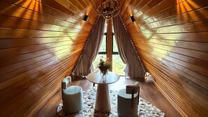 Habitació amb llistons de fusta, un penjoll, una taula rodona, dues cadires i una catifes geomètrica.