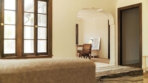 Una habitació amb una finestra gran, una porta de fusta, una cadira i un taulell amb un quadre.