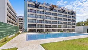 Ein modernes Gebäude mit Swimmingpool, mehreren Balkonen und einem grünen Zaun.