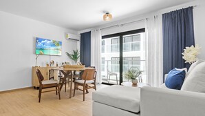 Ein Wohnzimmer mit einer Couch, einem Esstisch, Stühlen und einem großen Fenster mit Vorhängen.
