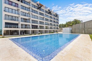 A modern building with a swimming pool, multiple balconies, and a parking area. - Modern 1BR w/2 Pools + Balcony Near Beach & Dining (Punta Cana)