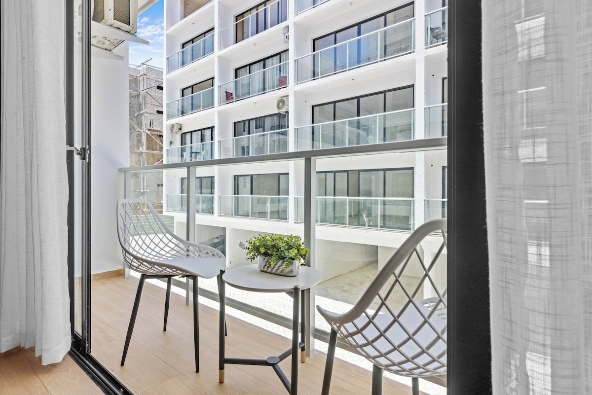 Un balcon doté d’une balustrade en verre, de deux chaises, d’une petite table et d’une plante en pot.