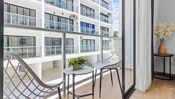 Ein modernes Hotelzimmer mit Balkon, Glasgeländern, einer Topfpflanze und einer Vase mit Blumen.