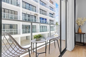 En modern hotellinredning med en balkong, en sittgrupp och utsikt över byggnadens fasad.