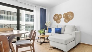 Ein modernes Wohnzimmer mit einer Couch, einem Esstisch, Stühlen und Blick auf ein Gebäude durch große Fenster.