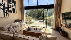 Ein modernes Wohnzimmer mit einer Couch, einem Couchtisch und großen Fenstern mit Blick auf einen Garten.