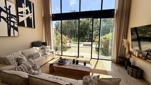 A modern living room with a sofa, coffee table, and large windows overlooking a garden. - Exclusive Villa: Stunning Rooftop Pool, Jungle Views, and Beach Concierge (Tulum)
