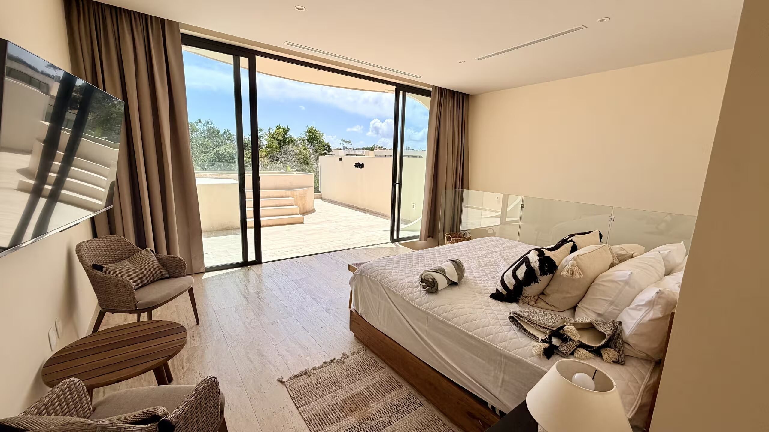 A hotel room with a bed, a chair, a TV, and a balcony with a view.