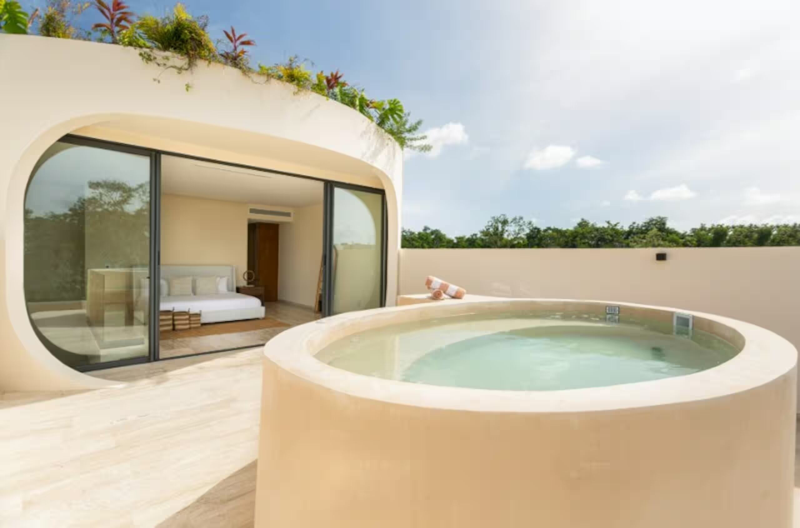 Une chambre d’hôtel moderne avec un mur en verre, un balcon privé et un jacuzzi.