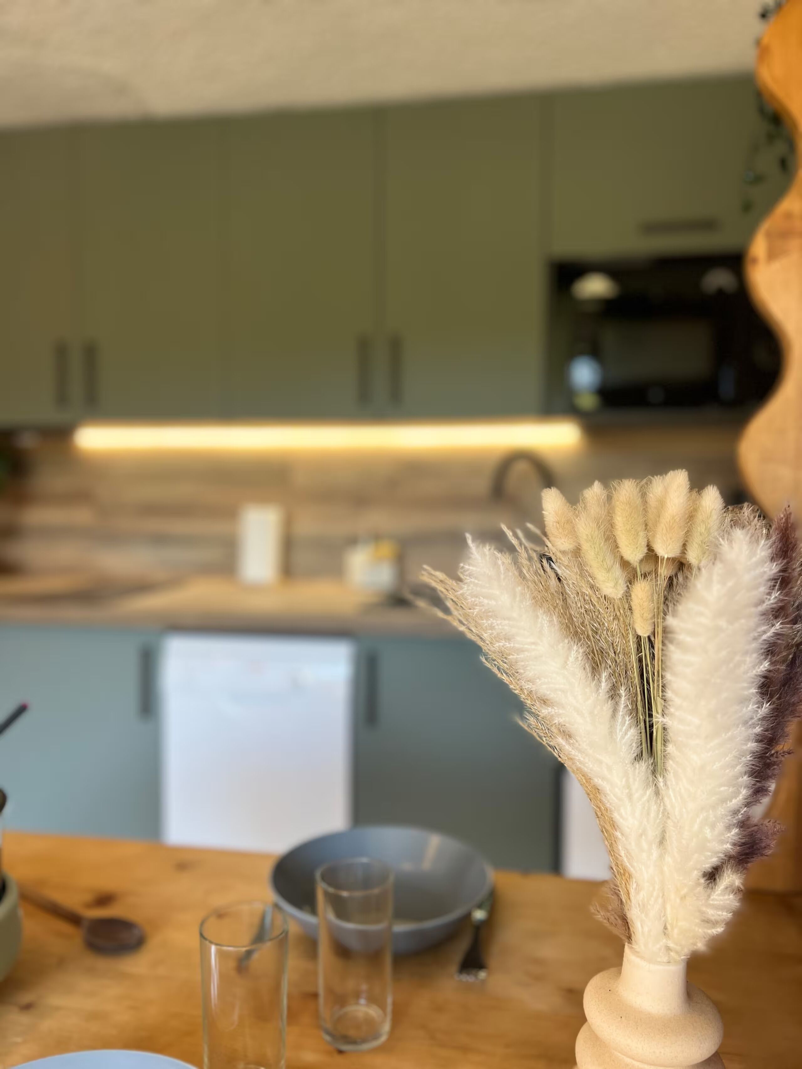 A kitchen with a dining table, a vase with dried pampas grass, and a microwave.