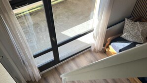 Een modern interieur met een houten vloer, een witte trap en uitzicht door een glazen deur op een buitenruimte.