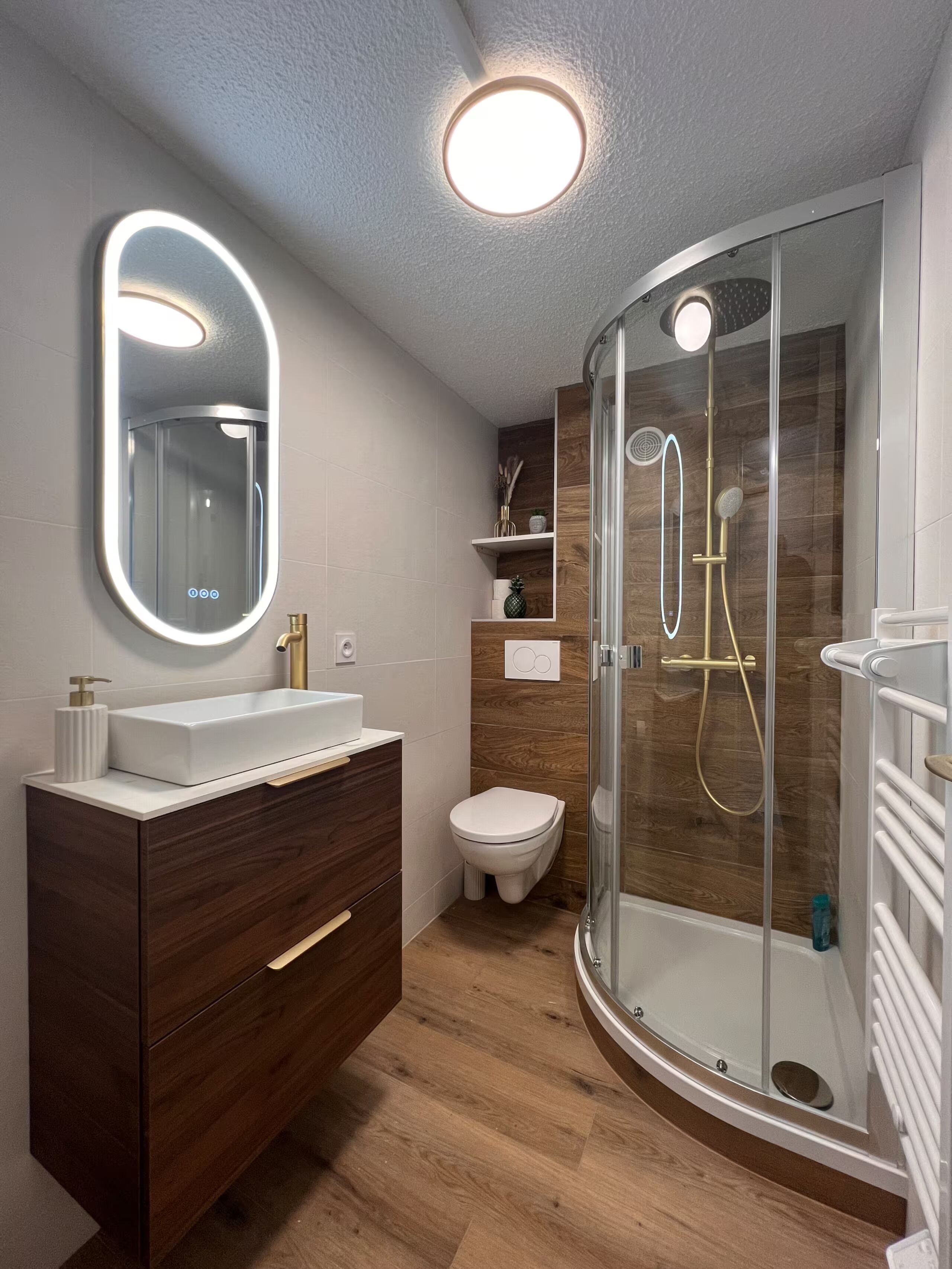 Une salle de bain moderne avec une douche à parois de verre, un lavabo blanc avec un miroir et des meubles en bois.