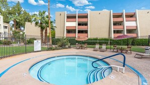 A swimming pool with a blue edge, surrounded by lounge chairs and umbrellas, with a building in the background. - 1BR Prime Old Town Condo with Resort Amenities! (Scottsdale)