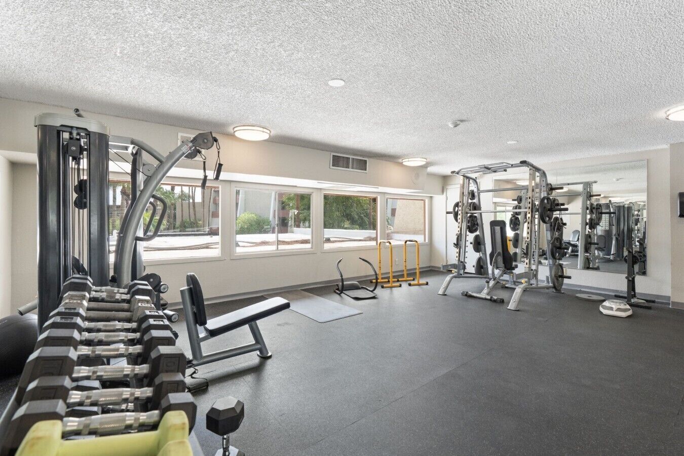A gym with weightlifting equipment, benches, and a mirrored wall.