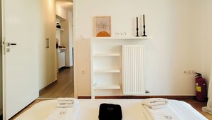 A hotel room with a bed, a radiator, a shelf with candles, and a fire extinguisher. - Modern Coastal Escape in Paleo Faliro (Paleo Faliro)