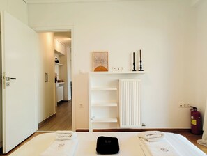 A hotel room with a bed, a radiator, a shelf with candles, and a fire extinguisher. - Modern Coastal Escape in Paleo Faliro (Paleo Faliro)