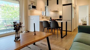 A modern kitchen with a dining area, a small refrigerator, and a window with a view of greenery. - Modern Coastal Escape in Paleo Faliro (Paleo Faliro)