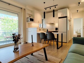 A modern kitchen with a dining area, a small refrigerator, and a window with a view of greenery. - Modern Coastal Escape in Paleo Faliro (Paleo Faliro)