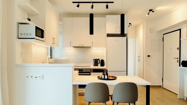 A modern kitchen with white cabinetry, a central island, two grey chairs, and a microwave above the counter. - Modern Coastal Escape in Paleo Faliro (Paleo Faliro)