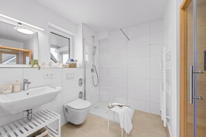 A modern bathroom with a sink, toilet, shower, and a small table with a towel. - Seeschwalbe - Balcony, parking space, wash-dryer, 3 TVs, infrared cabin (Olpenitz)