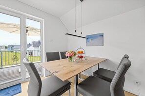A dining area with a wooden table, grey upholstered chairs, a vase with flowers, a fruit bowl, and a painting on the wall. - Seeschwalbe - Balcony, parking space, wash-dryer, 3 TVs, infrared cabin (Olpenitz)