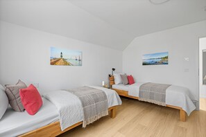 A bedroom with two single beds, a wooden floor, and two wall-mounted pictures. - Seeschwalbe - Balcony, parking space, wash-dryer, 3 TVs, infrared cabin (Olpenitz)