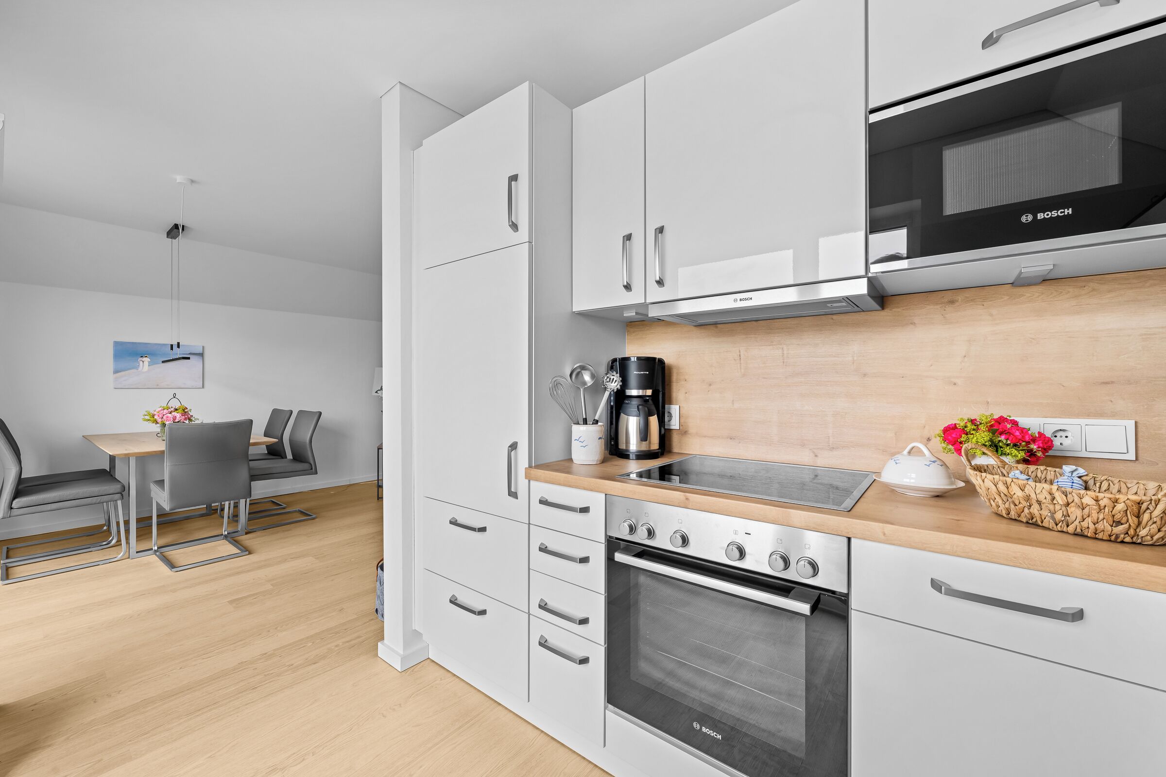 Una cocina moderna con armarios blancos, un microondas Bosch y una cafetera.