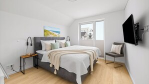 Une chambre moderne avec un lit, une table de chevet, une lampe et une vue sur l’extérieur.