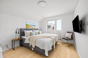A modern bedroom with a bed, bedside table, lamp, and a view of the outside. - Seeschwalbe - Balcony, parking space, wash-dryer, 3 TVs, infrared cabin (Olpenitz)
