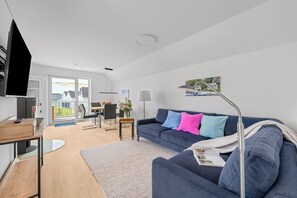 A modern living room with a sofa, coffee table, TV, and a dining area with chairs and a table. - Seeschwalbe - Balcony, parking space, wash-dryer, 3 TVs, infrared cabin (Olpenitz)