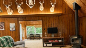 L’intérieur chaleureux d’un chalet avec des murs en bois, une cheminée, des têtes de cerf accrochées au mur, un téléviseur et un coin repas.
