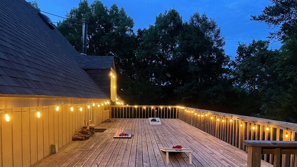 Une terrasse en bois agrémentée de guirlandes lumineuses, un espace abrité et un banc.