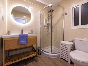 Ein Badezimmer mit Duschkabine, Waschbecken mit Holzschrank und Toilette.