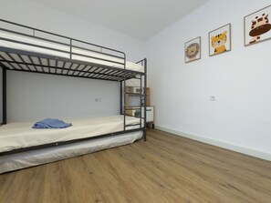 Quarto com beliche, piso de madeira, escrivaninha e prateleira fixada na parede.