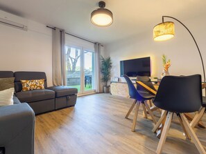 Uma sala de estar moderna com um sofá, mesa de jantar, cadeiras, uma TV e uma luminária no teto.