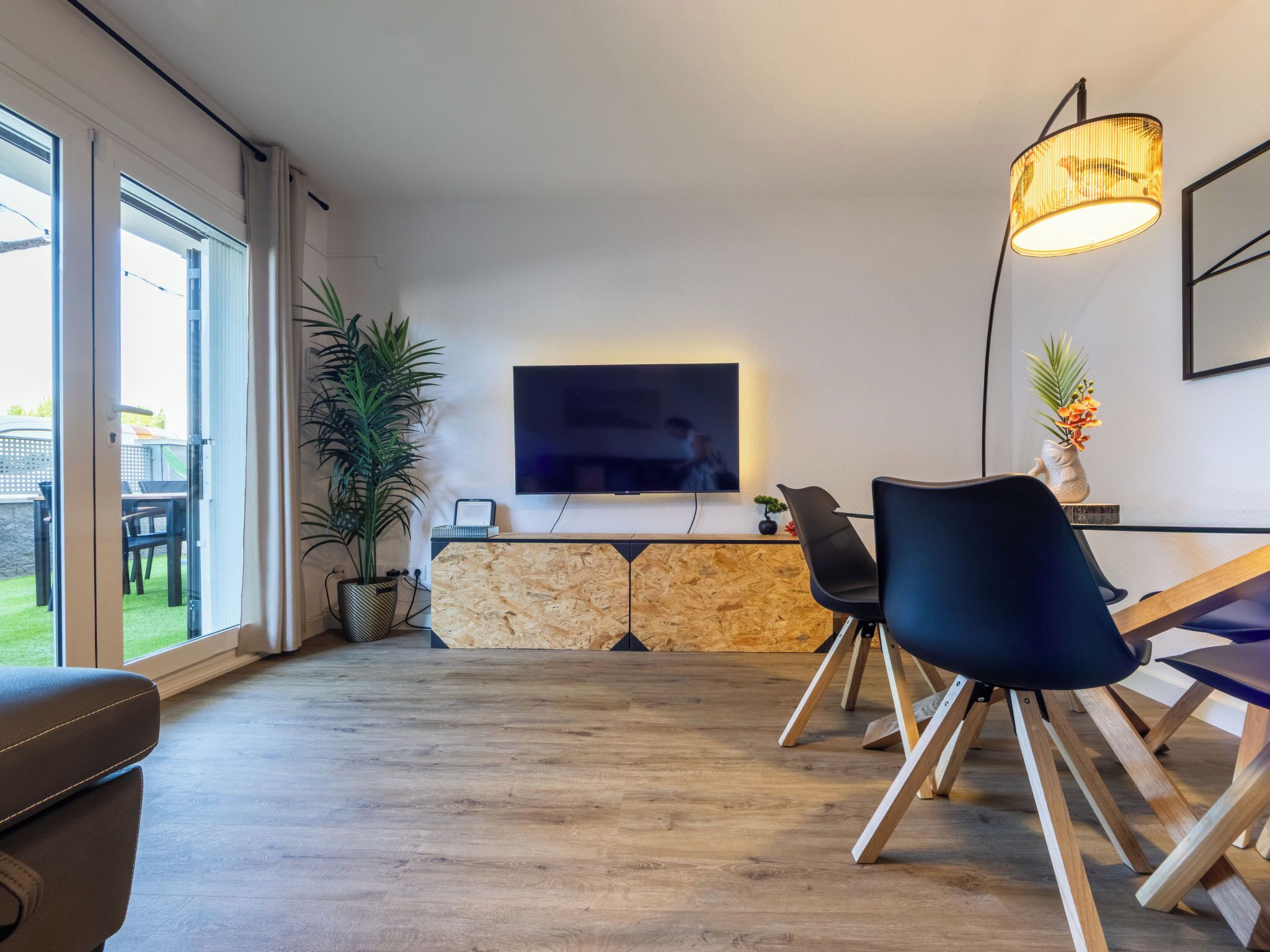 A modern living room with a flat-screen TV, a dining area with chairs, a potted plant, and a stone wall.