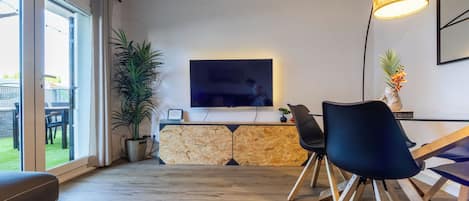 Una sala de estar moderna con televisor de pantalla plana, un comedor con sillas, una planta en maceta y una pared de piedra.