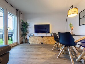 A modern living room with a flat-screen TV, a dining area with chairs, a potted plant, and a stone wall. - Rosa Dels Vents by Interhome (Cambrils)