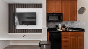 Eine moderne Küche mit Flachbildfernseher, Holzschränken, einer Mikrowelle und einem Edelstahl-Mülleimer.