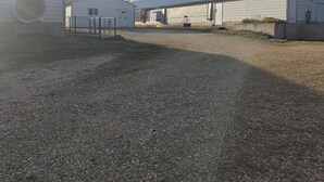 A gravel driveway leading to a row of white buildings with large windows and a circular structure on the left.