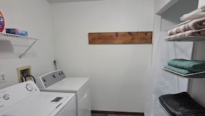 A laundry room with a washing machine, dryer, shelves with folded towels, and a wooden shelf.