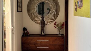 A hallway with a round mirror, wooden cabinet, and a painting on the wall. - COMFORT AND PEACE OF MIND (Remire-Montjoly)