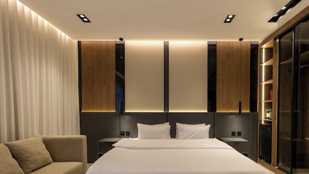 Habitació d'hotel moderna amb un llit gran, un sofà i una porta corredissa de vidre.