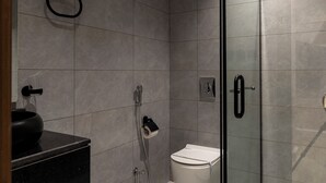Un baño moderno con cabina de ducha de vidrio, inodoro y encimera negra con lavabo.