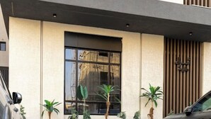 Fachada moderna de un edificio con un ventanal grande, persianas verticales y plantas en macetas.