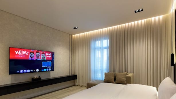 Una habitación de hotel moderna con una cama grande, un televisor de pantalla plana montado en la pared, una mesita de noche y una ventana con cortinas.