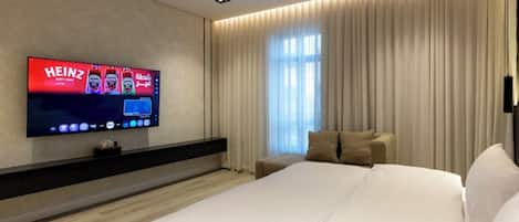 Una habitación de hotel moderna con una cama grande, un televisor de pantalla plana montado en la pared, una mesita de noche y una ventana con cortinas.