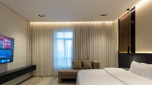 Habitació d'hotel moderna amb un llit gran, zona de seients, televisió plana penjada a la paret i un gran finestral amb cortines.
